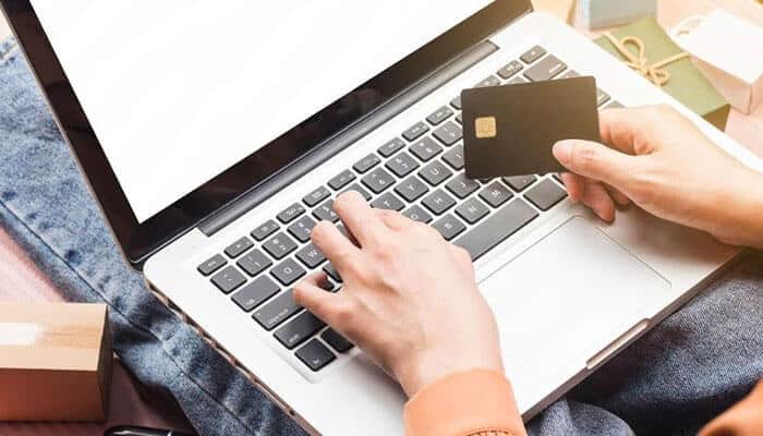 Why card type and method matter - tycoonstory | tycoonstory media Person typing on a laptop keyboard while holding a credit card, suggesting online shopping/checkout.