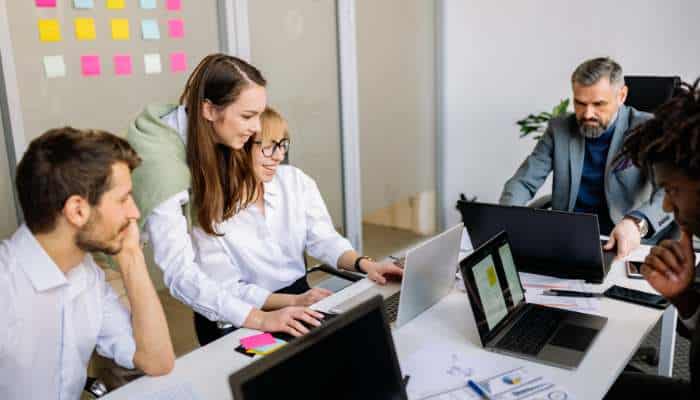 The business case for desktop-native collaboration in enterprise environments | tycoonstory media A group of five coworkers collaborates around a conference table, focused on laptops and documents.
