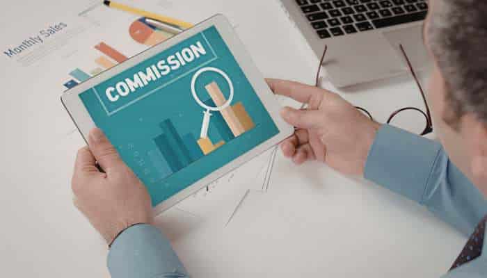 The commission model changing real estate careers 1 | tycoonstory media Tablet screen shows a 'commission' graphic with charts and a magnifying glass on a desk top.