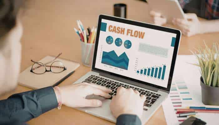 The hidden inefficiencies slowing down small business cash flow 1 | tycoonstory media Laptop screen showing a cash flow dashboard with charts and graphs on a cluttered desk.