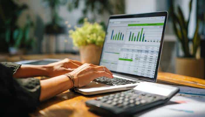 The metric most founders ignore on youtube 1 | tycoonstory media Hands typing on a laptop displaying green bar charts and financial data on a wooden desk.