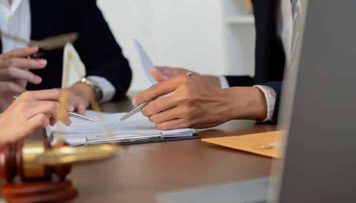 Trust litigation 1 | tycoonstory media Hands signing documents at a desk with papers, a gavel, and a folder in view.