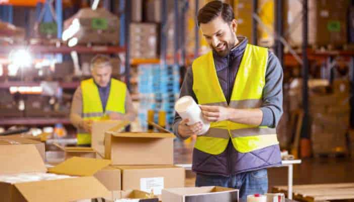 Ways 3pl kitting services streamline ecommerce growth 1 | tycoonstory media Two warehouse workers in yellow vests packing and inspecting boxes in a storage facility.