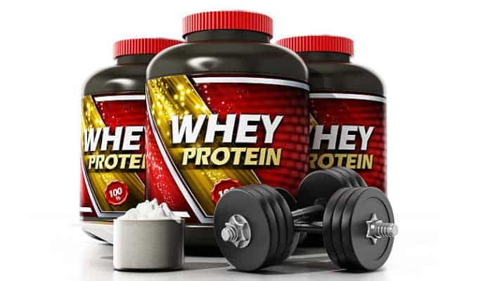 Whey protein powder 1 | tycoonstory media Three whey protein containers with red caps and bold labels, a measuring scoop, and a dumbbell set on a white background, shot for a fitness product image.