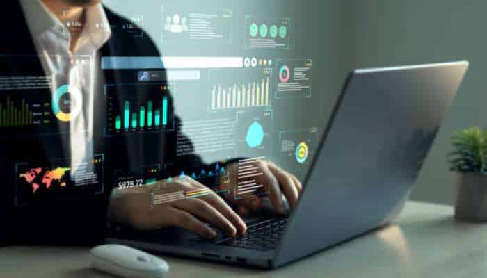 Why businesses are switching to digital clm software 1 | tycoonstory media Businessperson typing on a laptop with holographic analytics dashboards and charts.
