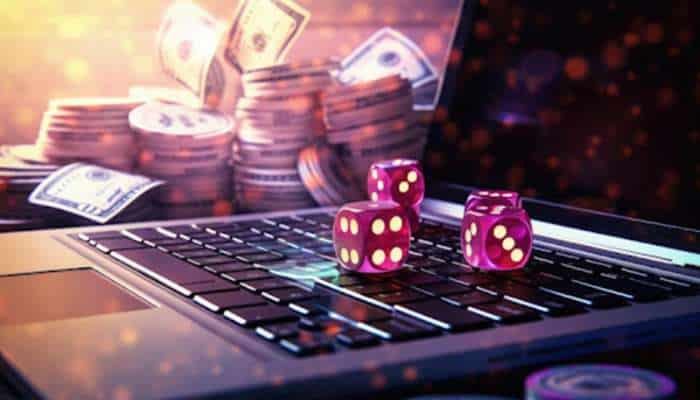 Why online casinos continue to attract new players 1 | tycoonstory media Purple dice sit on a laptop keyboard with piles of coins and scattered dollar bills in the background, signaling online gambling.