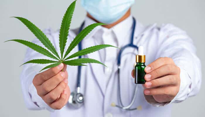Clarify thc details and regional requirements - tycoonstory | tycoonstory media Medical professional in a white coat with mask showing a cannabis leaf and a small bottle of cannabis oil.