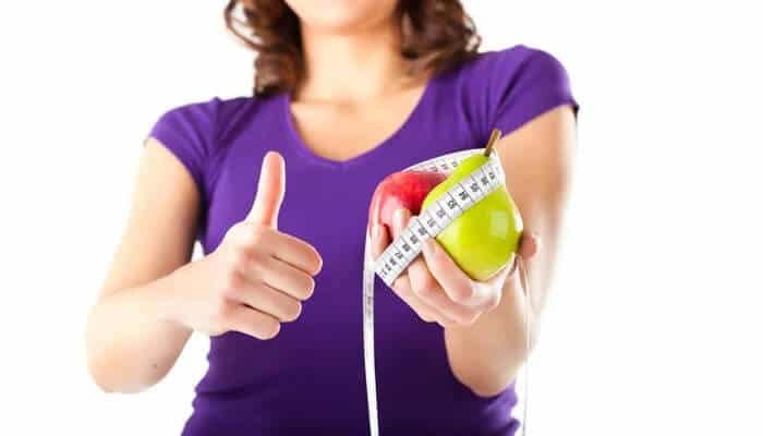 The benefits extend well beyond weight loss - tycoonstory | tycoonstory media Person in a purple shirt gives a thumbs-up while holding a green apple wrapped with a measuring tape, symbolizing healthy eating and fitness.