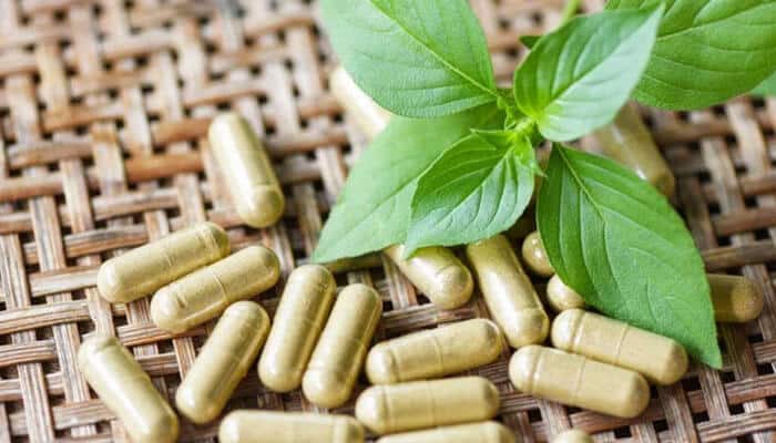 Prenetics im8 daily ultimate essentials pro - tycoonstory | tycoonstory media Gold capsules scattered on a woven mat with fresh green herb leaves, suggesting herbal supplements.
