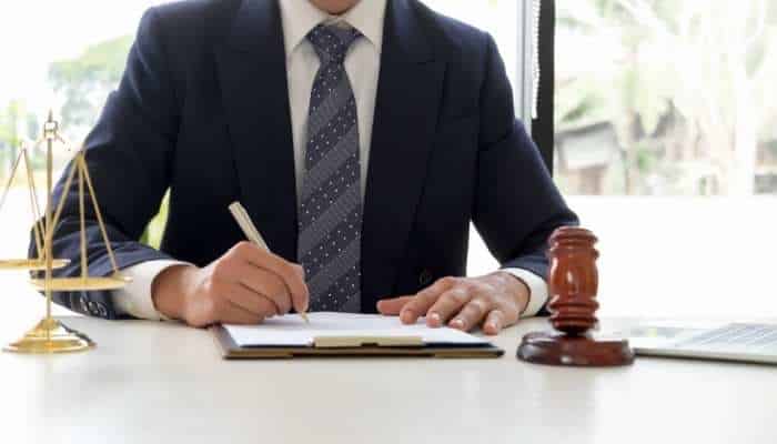 3 highly rated philadelphia pa personal injury law firms 1 | tycoonstory media Lawyer in a dark suit signs a document at a desk, with a gavel and scales of justice nearby.