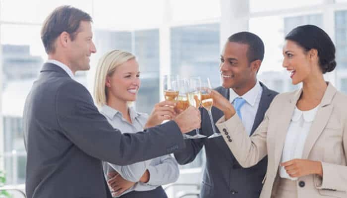 Reducing pressure to drink - tycoonstory | tycoonstory media Four professionals in business attire raising glasses in a toast in a bright office setting.