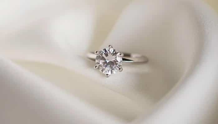 Judge the diamond as a whole - tycoonstory | tycoonstory media Close-up of a solitaire diamond engagement ring on white satin fabric.
