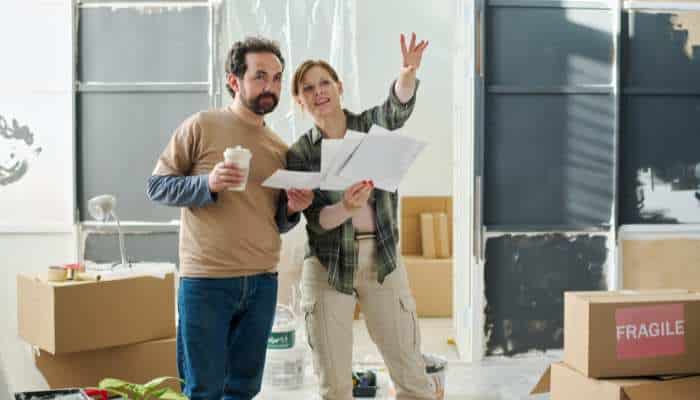 Budget-friendly ideas to refresh your home 2 | tycoonstory media Couple in a partly finished room reviewing plans, surrounded by moving boxes and supplies.