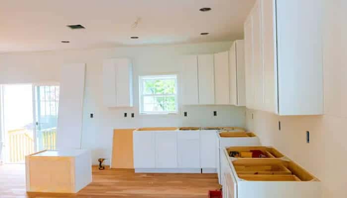 Lighting upgrades | tycoonstory media White kitchen cabinets under construction, drawers open, plywood countertops, and exposed wiring walls.