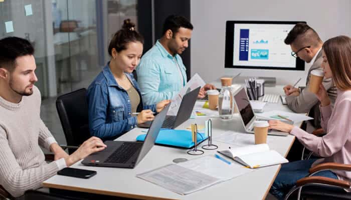 The 7 best digital marketing agencies in perth for 2026 | tycoonstory media Five professionals work around a white table with laptops, papers, and coffee cups in a modern office.