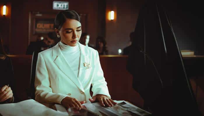 Consider knowledge of new york laws | tycoonstory media Woman in a white blazer sits at a table, looking over a newspaper in a dimly lit lounge.