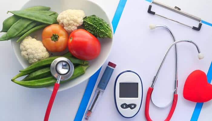 What are the factors responsible for high cholesterol levels? - tycoonstory | tycoonstory media Bowl of fresh vegetables with a stethoscope, a glucose meter, and a clipboard on a white surface, signaling health and nutrition.