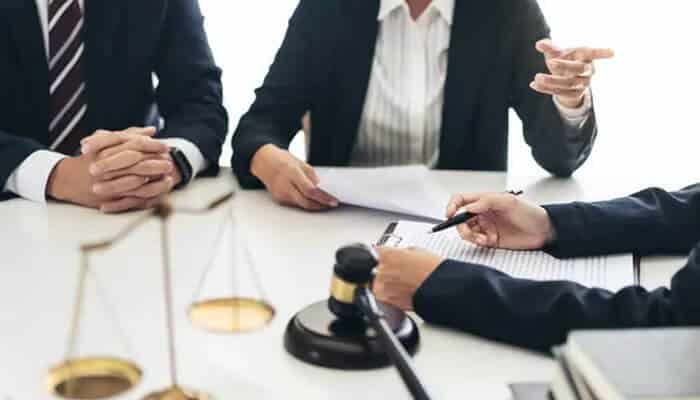 Understanding the real long-term costs of a conviction - tycoonstory | tycoonstory media Lawyers in suits at a table with a gavel and scales, discussing documents in a legal meeting.