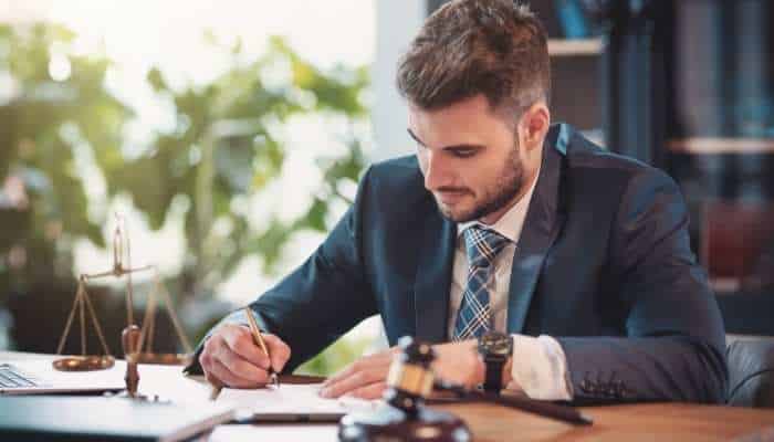 How accident attorneys respond when an insurer disputes injuries 1 | tycoonstory media A lawyer in a navy suit signs documents at a desk, with a gavel and scales of justice nearby.