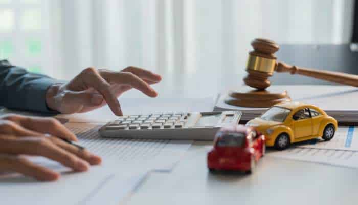 How car crash attorneys protect clients from hidden policy traps 1 | tycoonstory media Person using a calculator beside documents on a desk, with a judge's gavel and toy cars nearby, suggesting auto insurance or legal work.