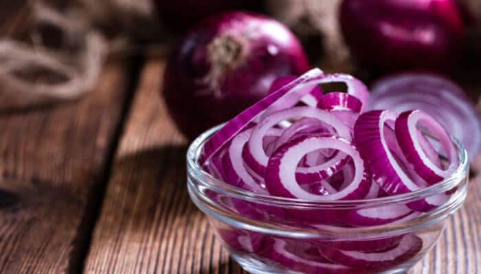 How much raw onion is too much - tycoonstory | tycoonstory media Disadvantages of eating raw onion: freshly sliced red onion rings in a glass bowl, highlighting potential digestive issues such as bloating, gas, acid reflux, heartburn, fructan intolerance, and ibs symptoms that may occur from excessive raw onion consumption.