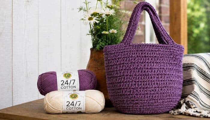 Is lion brand 24 7 cotton yarn good for bags - tycoonstory | tycoonstory media Lion brand 24/7 cotton yarn in purple and cream beside a structured crocheted tote bag, showcasing the mercerized cotton yarn’s crisp stitch definition.