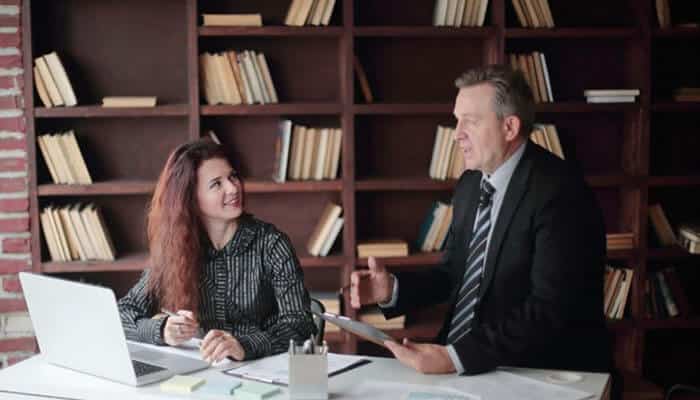 Devkota law firm llc - tycoonstory | tycoonstory media Two professionals discuss documents at a white desk in a library-like office, laptop open beside them.
