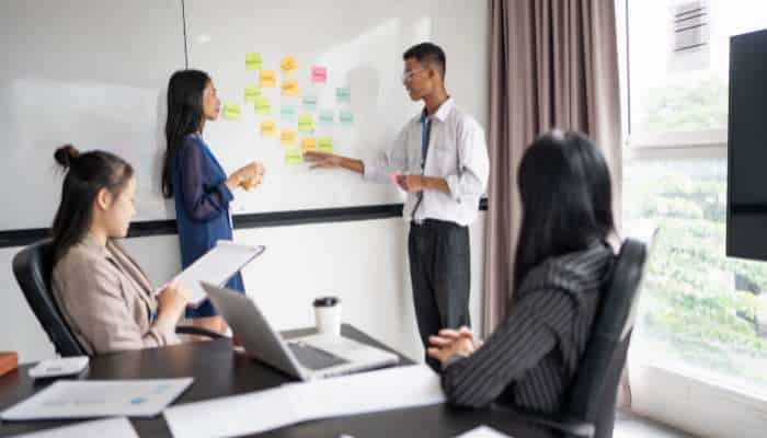 The founders cognitive edge 1 | tycoonstory media Two presenters discuss ideas at a whiteboard covered with colorful sticky notes while three coworkers listen in a bright meeting room