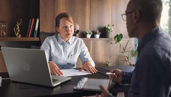The law offices of norka m. Schell, llc - immigration law guidance - tycoonstory | tycoonstory media Two colleagues in an office meeting at a desk: woman seated with a laptop and papers, man facing her while discussing.