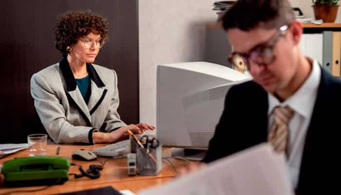 Montgomery law firm - tycoonstory | tycoonstory media Businesswoman in a gray blazer at a desk, typing on a desktop computer while a man in the foreground reads papers.