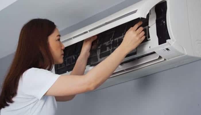 Myth: air conditioners only cool your air - tycoonstory | tycoonstory media Woman performing maintenance on a wall‑mounted air conditioner, with her hands reaching into the open front panel.