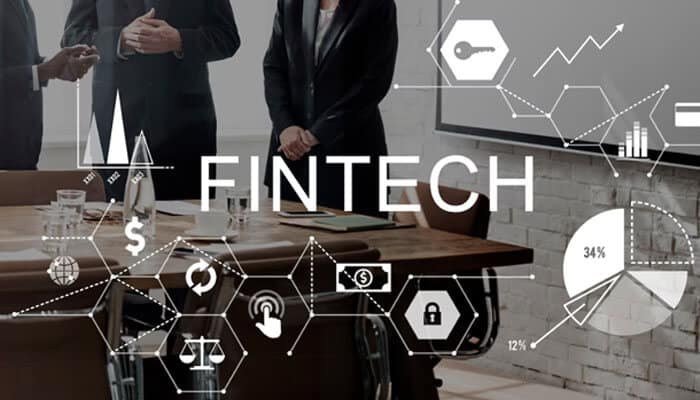 Powered by search - tycoonstory | tycoonstory media Businesspeople in a meeting with digital finance icons and the word fintech overlay, illustrating financial technology concepts.