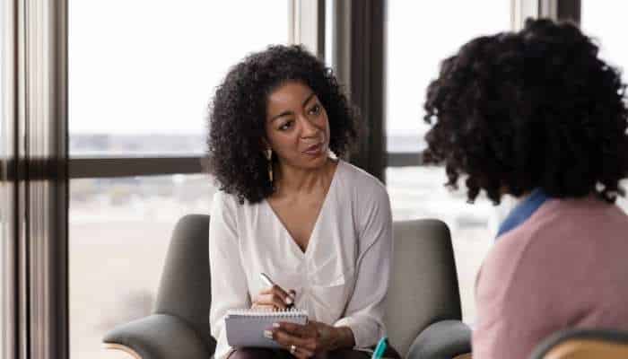 _a family guide to teen residential mental health treatment 1 | tycoonstory media Counselor with curly hair taking notes in a therapy session, speaking with a client.