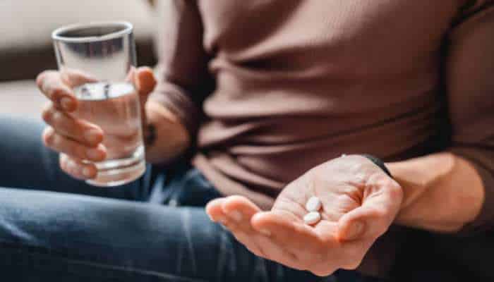 Armodafinil for beginners | tycoonstory media Person holding three white pills in one hand and a glass of water in the other.