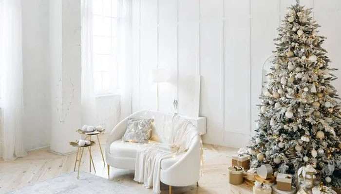 Use vertical space for holiday decorations | tycoonstory media White living room with a frosted christmas tree and wrapped presents beside a white sofa.