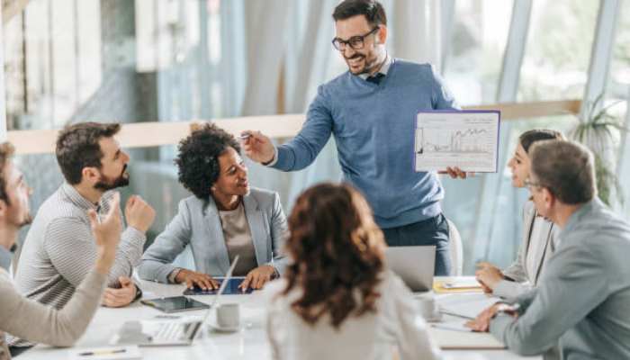Crypto teams are building multi-model ai stacks and the complexity is starting to show 1 | tycoonstory media Man in a blue sweater presents a chart to colleagues around a glass-walled conference table.