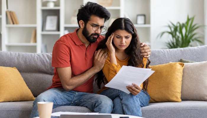 Raising your deductible helps, but only if you can actually pay it | tycoonstory media Couple sits on a gray sofa, looking worried as they read a document together.