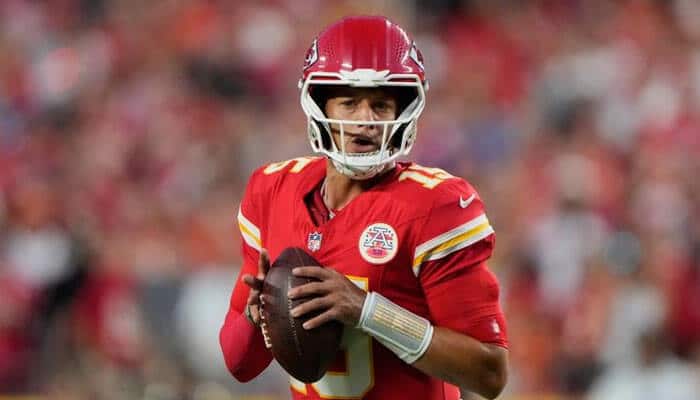 Sunday night football | tycoonstory media American football quarterback in a red uniform grips a football, ready to throw during a game with a crowded stadium in the background.