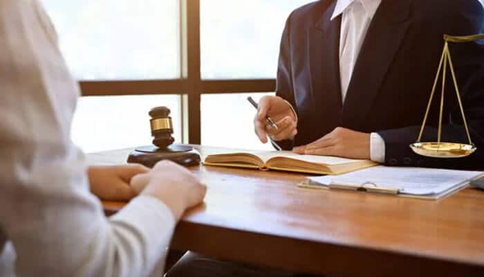 What to look for in a los angeles employment lawyer | tycoonstory media Lawyer in a suit writing at a desk with a gavel and scales of justice nearby on the table.