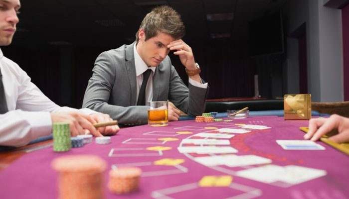 Why leadership matters more than luck in gambling | tycoonstory media Two men in suits sit at a casino poker table, concentrating as chips, cards, and a drink are spread across the green felt.