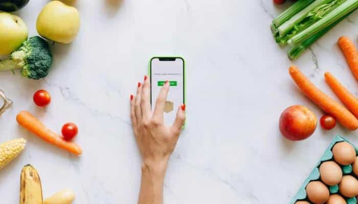 What k-diet users are saying | tycoonstory media Top‑down view of a hand tapping a green button on a smartphone screen, surrounded by fresh vegetables and eggs, symbolizing online grocery shopping.