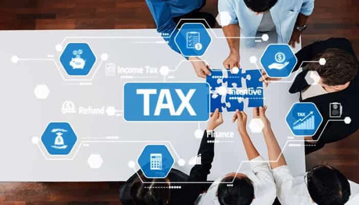 The 6 best international tax compliance experts for us expats in 2026 - tycoonstory | tycoonstory media Overhead view of professionals collaborating around a board with a central tax tile and finance icons.