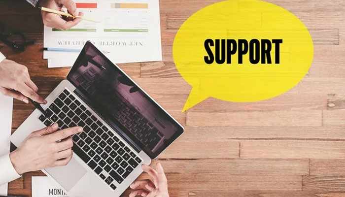 Support that goes beyond the consultation | tycoonstory media Hands typing on a laptop at a wooden desk with documents, a yellow speech bubble reading support.