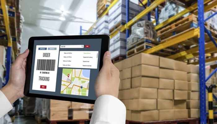 Reservety - best for operators managing multiple pickup locations or warehouses | tycoonstory media Person holding a tablet displaying an order tracking screen with a barcode, map, and order details in a warehouse venue.