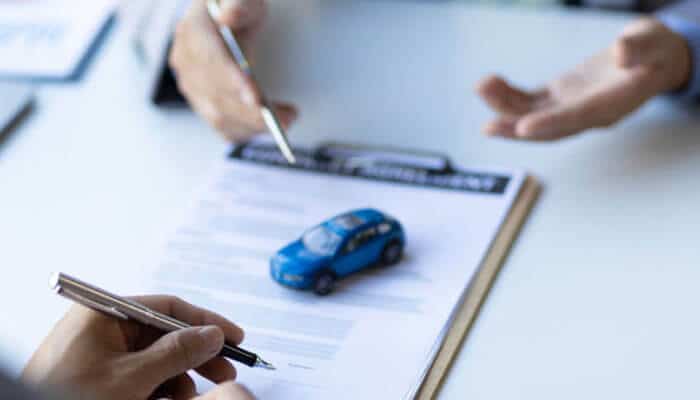 Look beyond the monthly premium | tycoonstory media Car insurance policy document review with vehicle model and customer discussing coverage options for better protection.