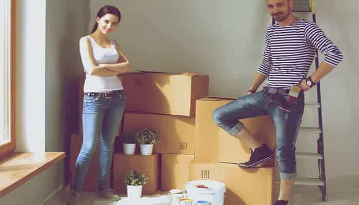 Take advantage of vertical space | tycoonstory media A couple stands in a room with several packed cardboard boxes, suggesting they are moving in together at a new home.