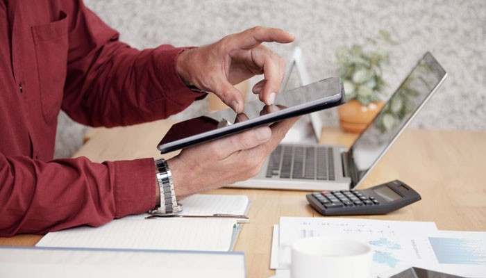 The 8 best virtual accounting companies for u. S. Businesses in 2026 | tycoonstory media Person in a red shirt uses a tablet while working at a desk with a laptop, calculator and papers nearby