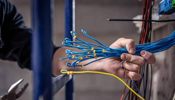 Key benefits of flexible cables - tycoonstory | tycoonstory media Technician's hand gathering blue ethernet cables with yellow zip ties near a network panel, showing cable management work