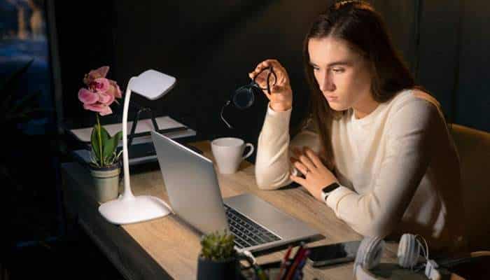 Smaller ai models are taking on more routine work | tycoonstory media Woman records a podcast at a desk with a laptop, microphone, and headphones in a dimly lit setup.