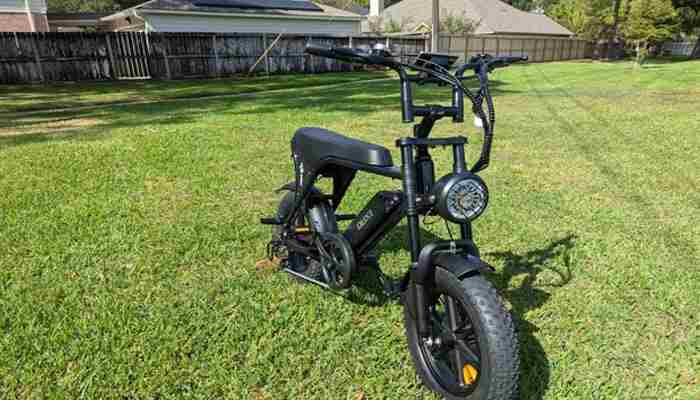 Parents can teach judgment, not just technique | tycoonstory media Black electric bike parked on a grassy backyard with a wooden fence and houses in the background, front light visible on the handlebar area.